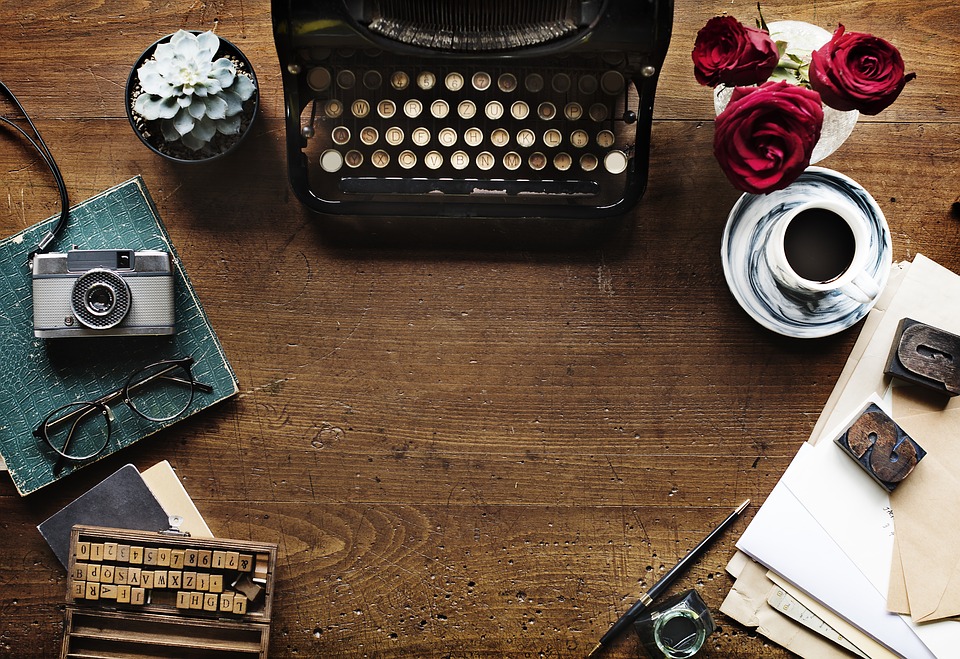 Top-down view of a desk top cluttered with a typewriter, coffee mug, old camera, and other knickknacks
