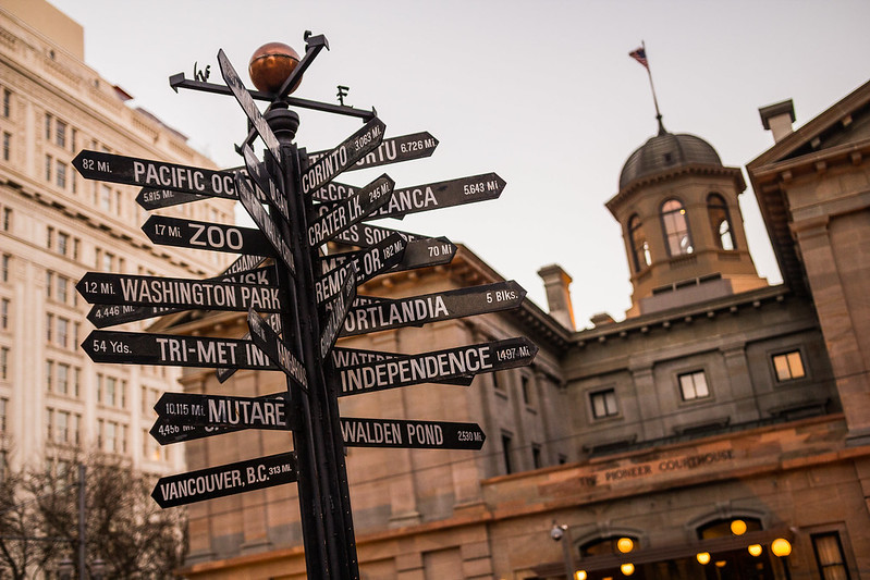 A sign post in the Pioneer Courthouse Square in Portland, OR pointing in several different directions.